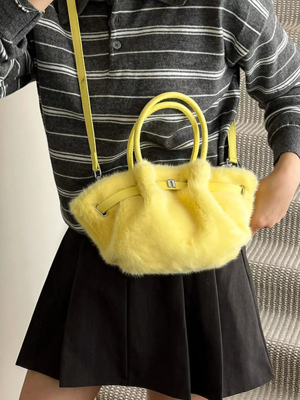 Yellow plush crossbody bag with chic buckle and top handles, styled with a striped shirt and black skirt.