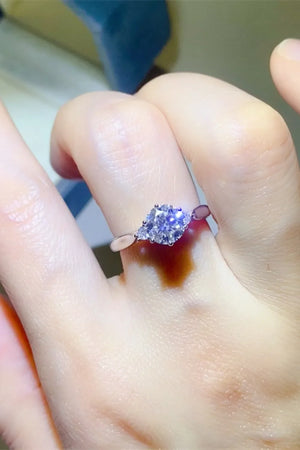 Silver moissanite trilogy engagement ring with a central round cut stone and two pear cut side stones.