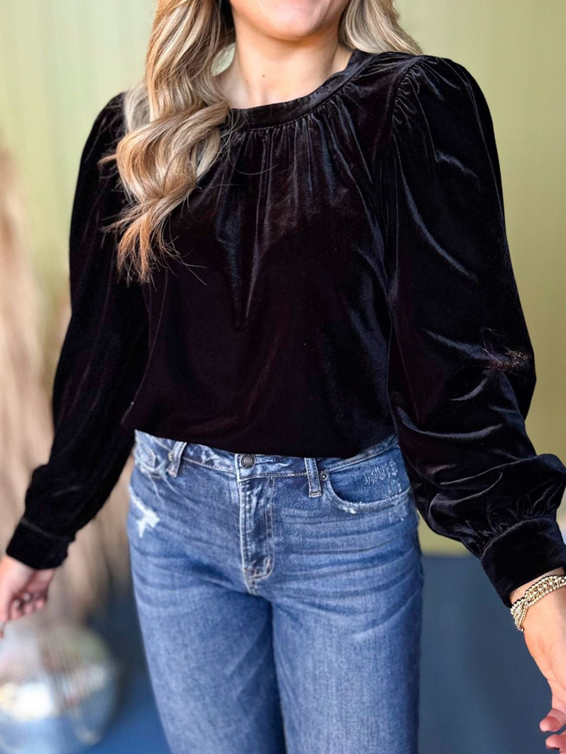 Black velvet blouse with ruched neckline and long puff sleeves, styled with jeans.