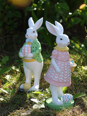 Easter bunny figurines in blush pink and gum leaf green, holding decorative eggs.