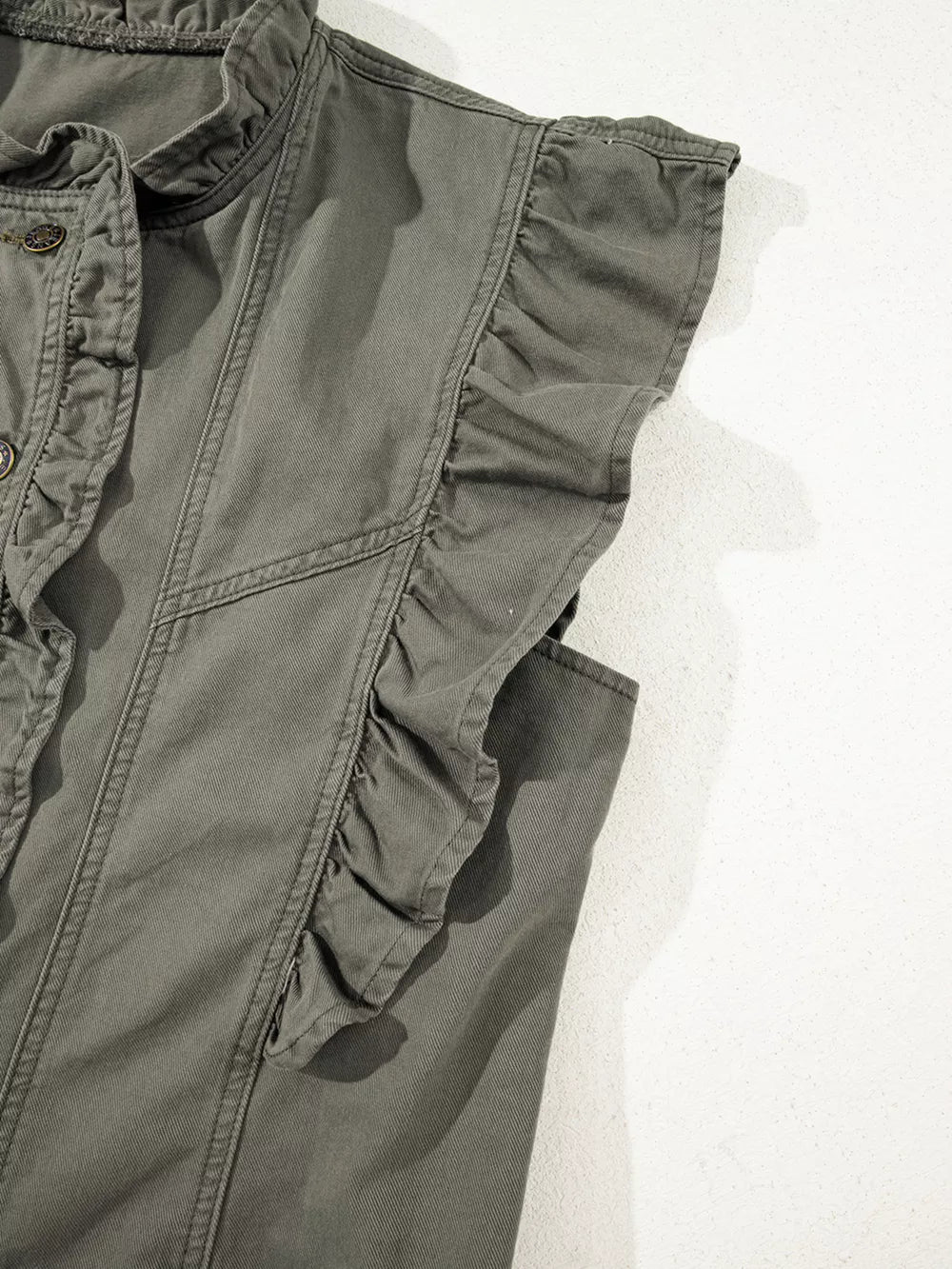 Ruffled denim vest with button closure and ruffled trim on sleeves.