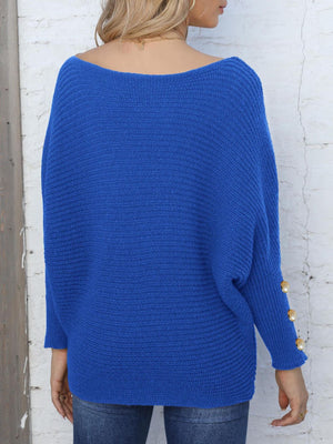 Royal blue batwing knit sweater with boat neck and pearl cuff details.