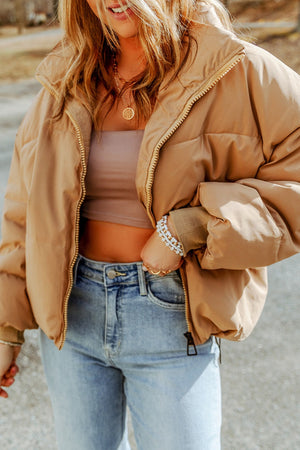 Tan padded crop jacket with stand collar and zip front, styled with jeans.