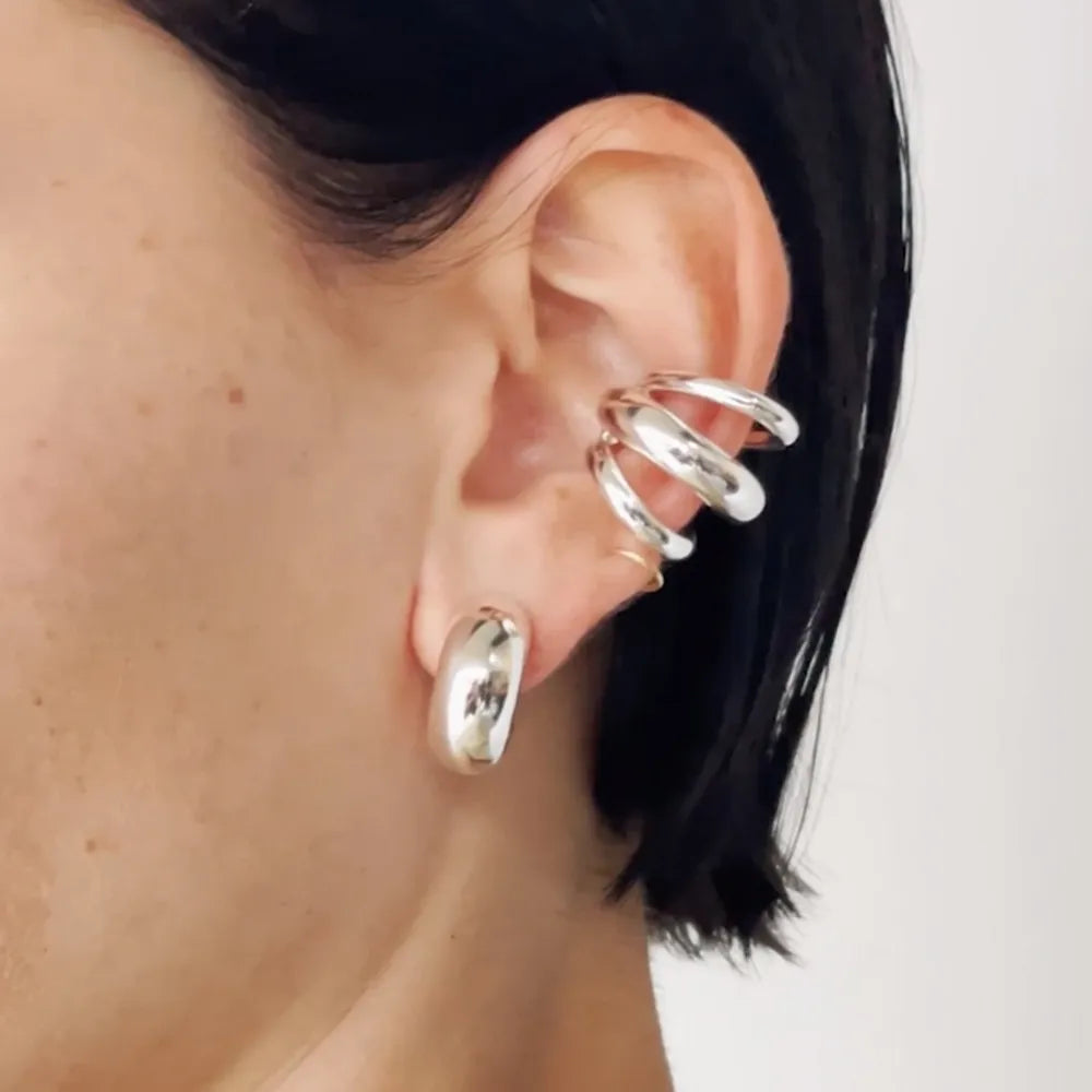 Silver sculptural ear cuff and hoop earrings with a modern, artistic design.