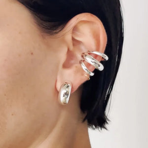 Silver sculptural ear cuff and hoop earrings with a modern, artistic design.