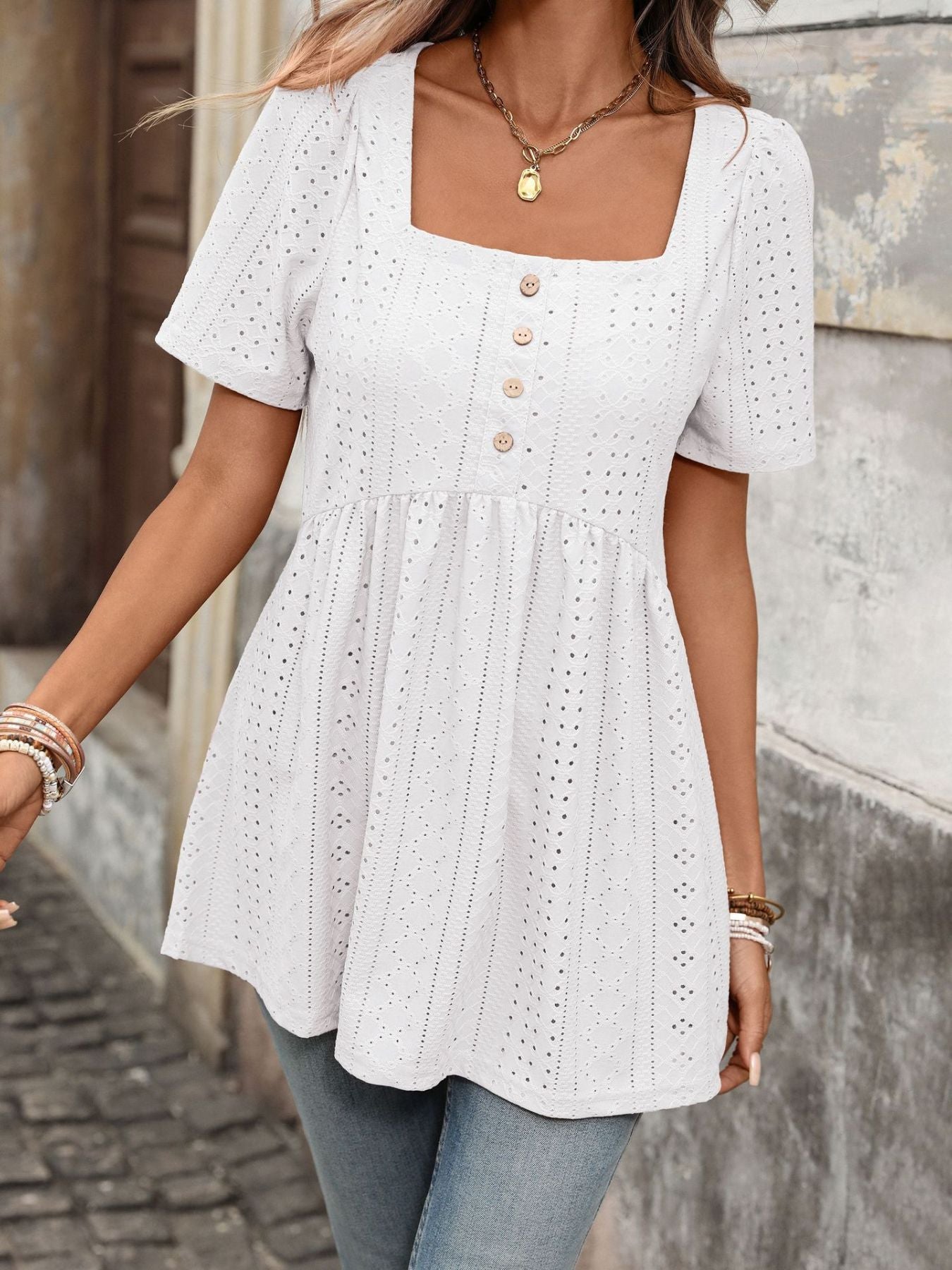 White eyelet babydoll top with square neck, puff sleeves, and decorative buttons.