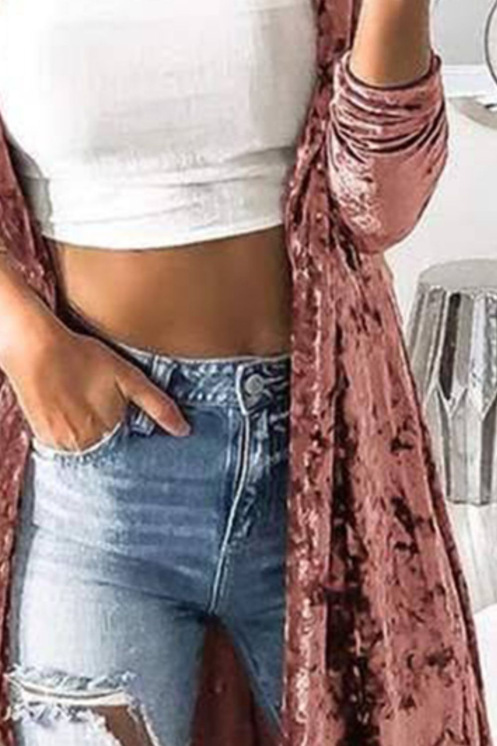 Pale blush crushed velvet duster coat with long sleeves and open front, styled with a white crop top and distressed jeans.