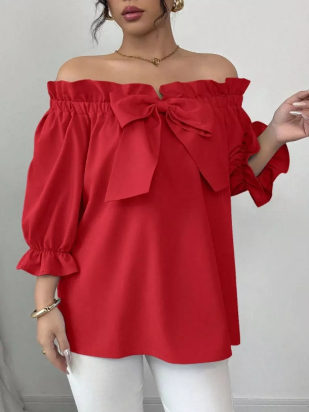 Red off-the-shoulder blouse with ruffled neckline and large bow detail.