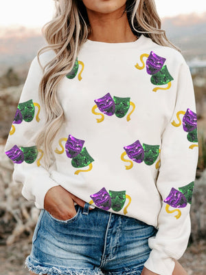White crewneck sweatshirt with all-over purple and green sequin mask motif and yellow ribbon accents.