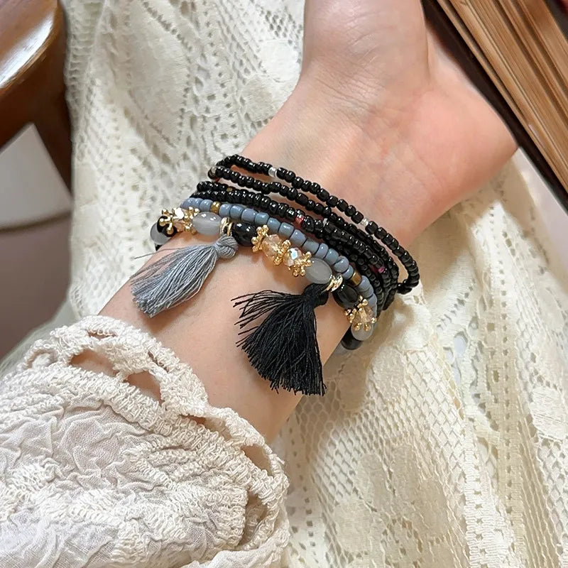 Beaded tassel stacked bracelet set with black, grey, and bronze beads and gold accents.