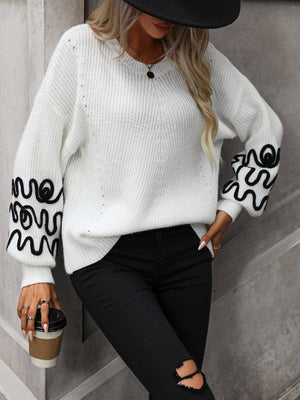 White knit sweater with voluminous sleeves featuring black embroidered wavy pattern detail.