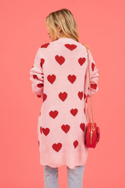 Blush pink acrylic longline cardigan with red heart pattern and ribbed trim.
