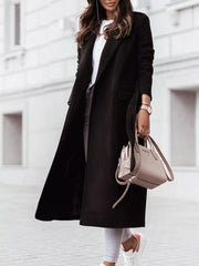 Black belted longline trench coat with flap pockets and lapel collar.