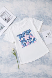White graphic tee with floral accents and "be kind" text, casual short sleeve.