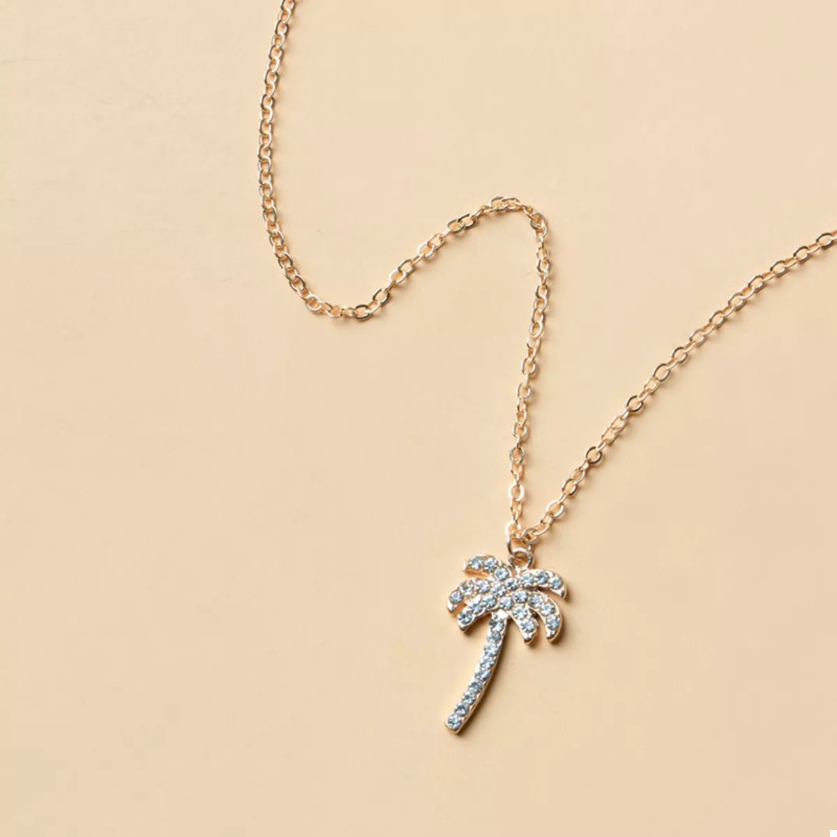 Gold palm tree pendant necklace with crystal accents on a delicate chain.