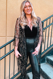 Black sequin duster with flared sleeves and fringe detail, worn over a black top and pants.