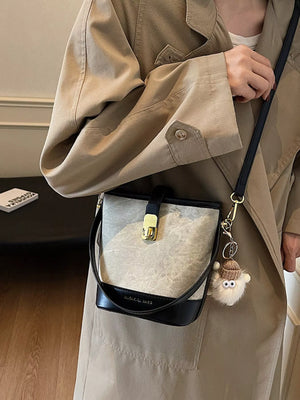 Elegant PU leather bucket bag in white with brown and black accents, featuring a gold clasp and fuzzy charm.