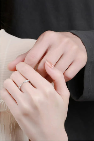 Delicate silver band ring with small stones, worn on a hand.
