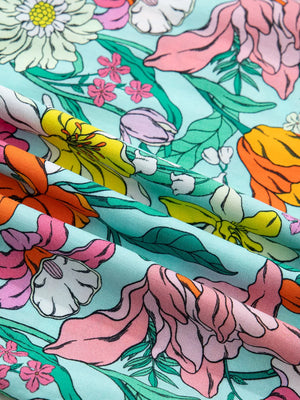 Maternity overshirt with vibrant floral print in pink, orange, yellow, and purple on a light blue background.