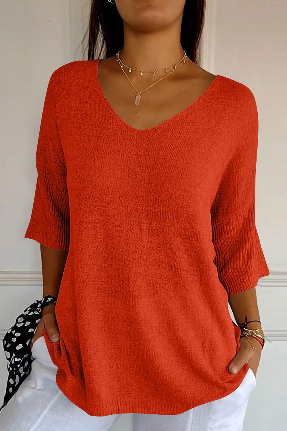 Red knit sweater with V-neck and flared sleeves, textured fabric.