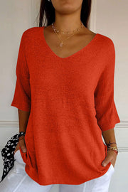 Red knit sweater with V-neck and flared sleeves, textured fabric.