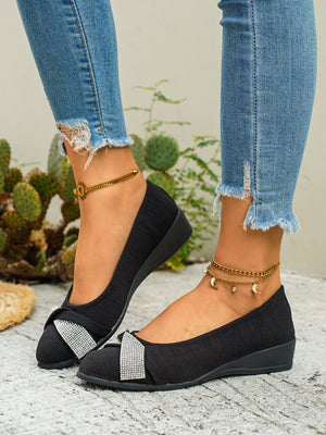 Black slip-on wedge flats with rhinestone bow detail.