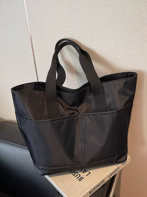 Black Oxford cloth shoulder tote bag with exterior pockets and double handles.