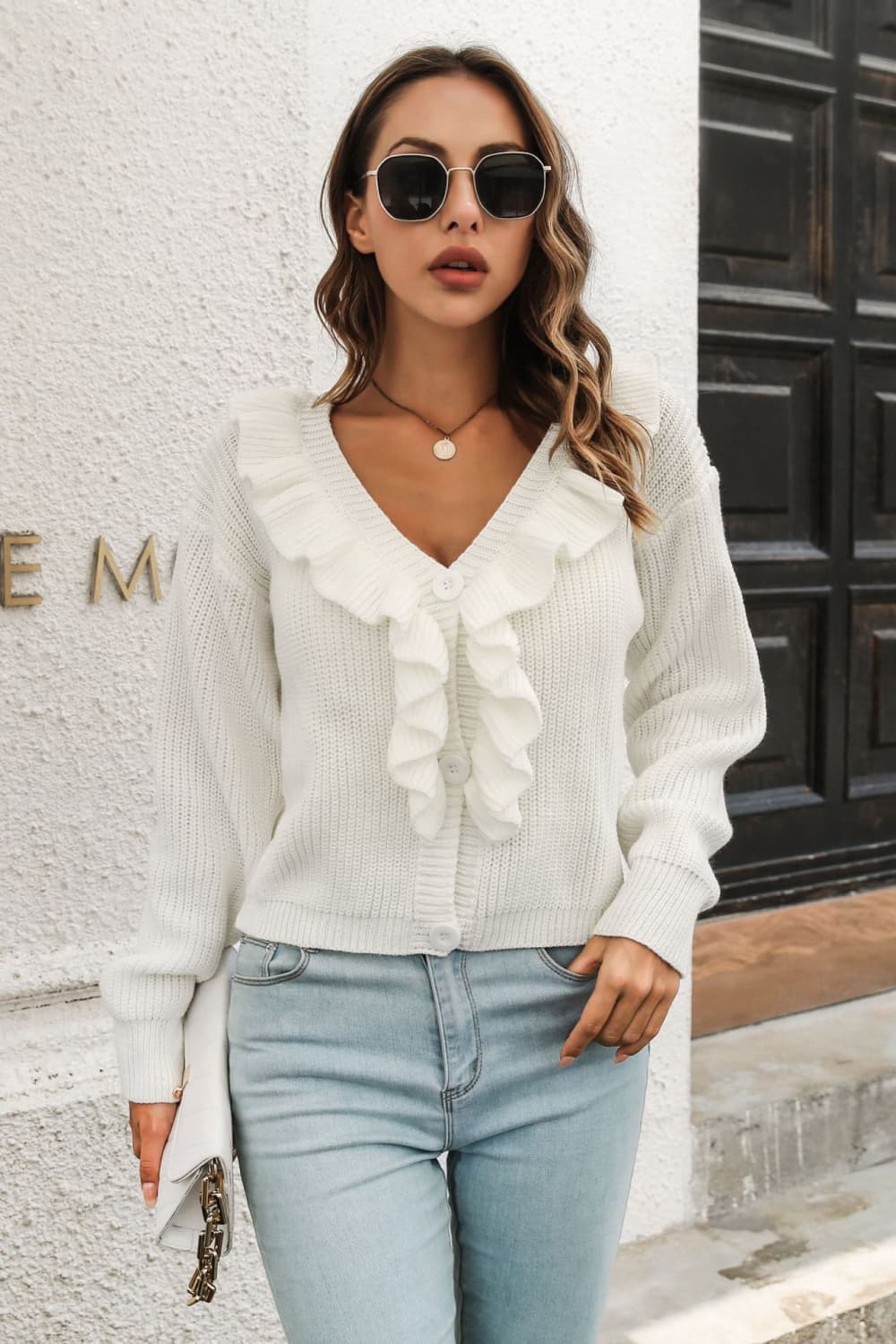 White knit cardigan with ruffled collar and button front, styled with jeans.