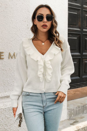 White knit cardigan with ruffled collar and button front, styled with jeans.