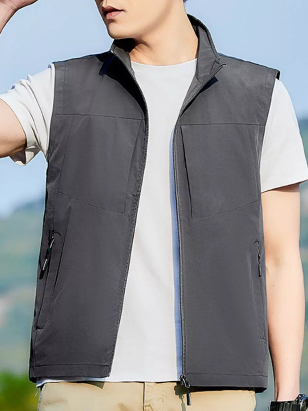 Men's grey zip up vest with stand collar and zippered pockets, worn over a white t-shirt.
