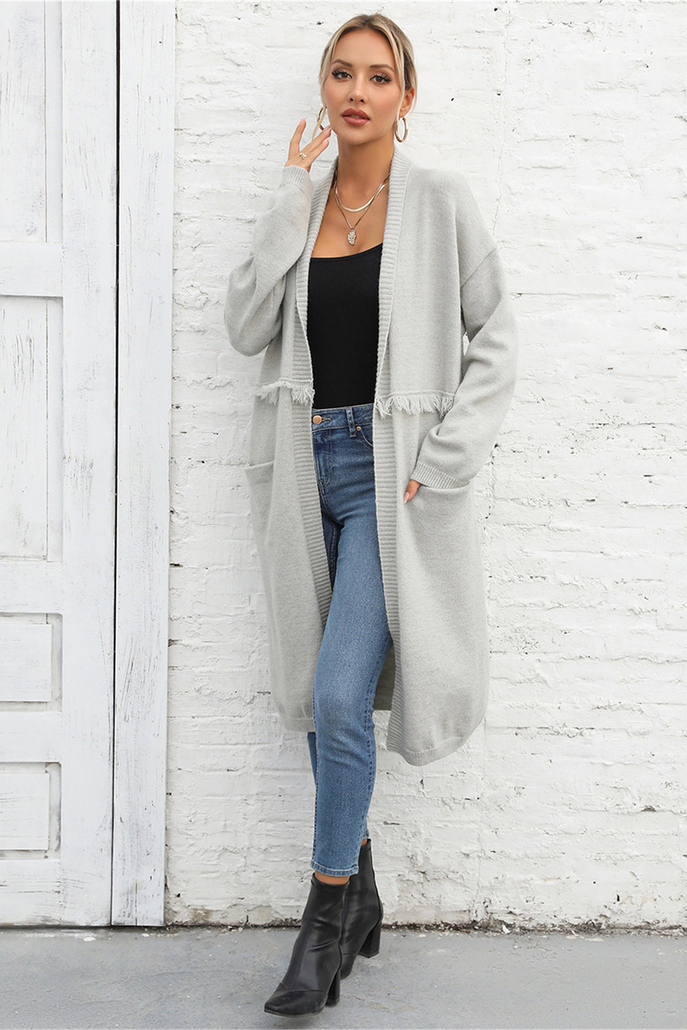 Light gray longline knit cardigan with fringe trim and pockets, open front, long sleeves.