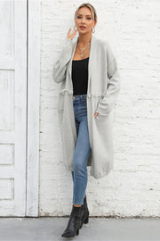 Light gray longline knit cardigan with fringe trim and pockets, open front, long sleeves.