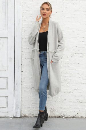 Light gray longline knit cardigan with fringe trim and pockets, open front, long sleeves.