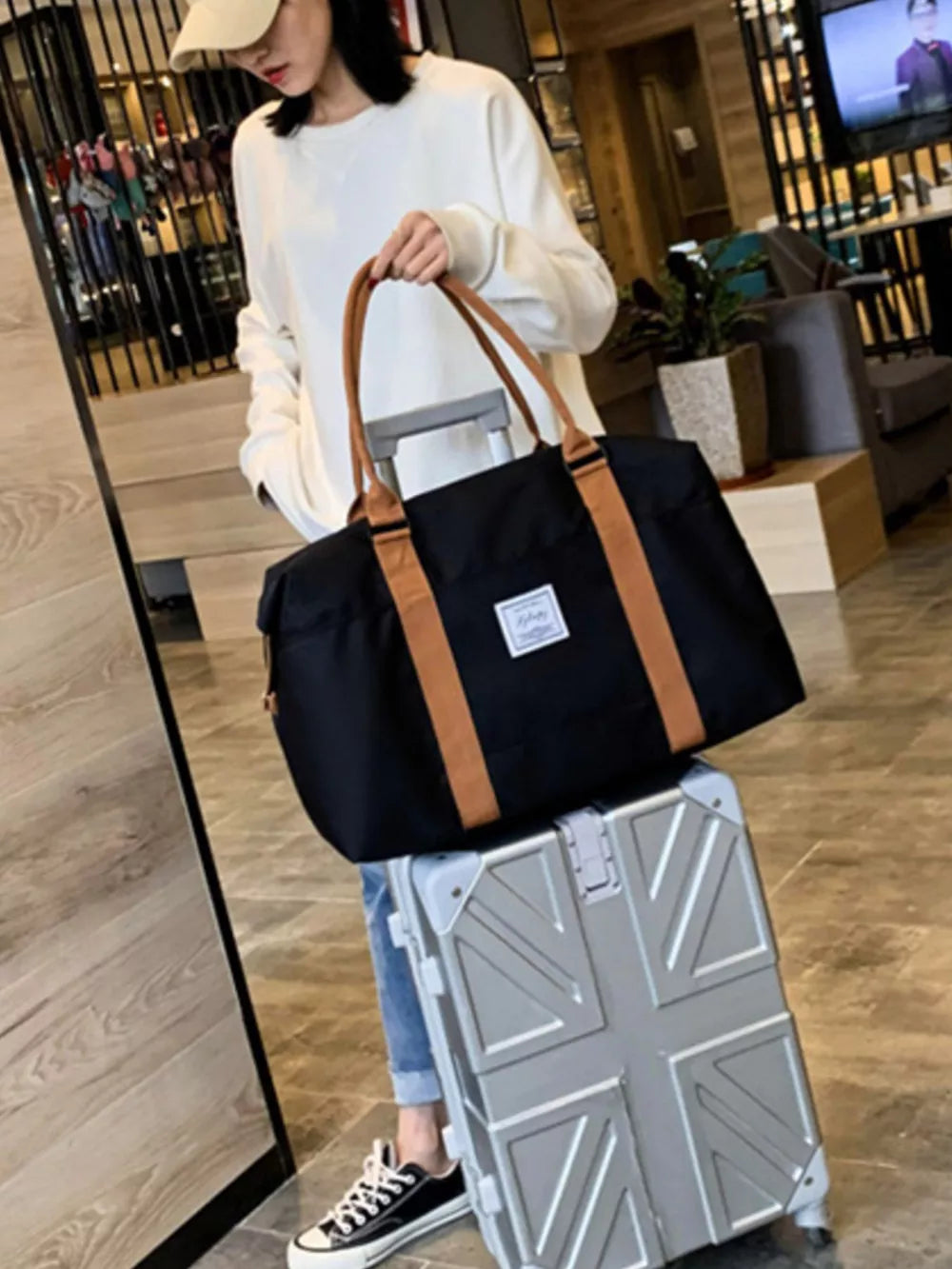 Large black Oxford cloth travel bag with tan contrast straps and white label, held by a woman.