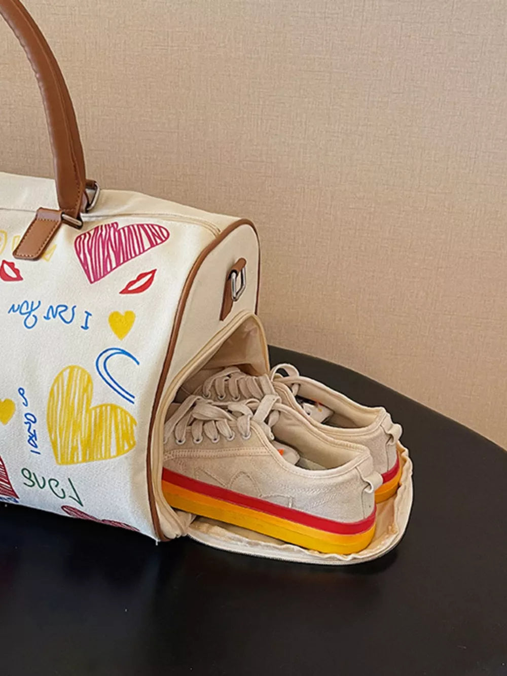 Vibrant canvas duffel bag with colorful heart print and brown trim, showing shoes inside.
