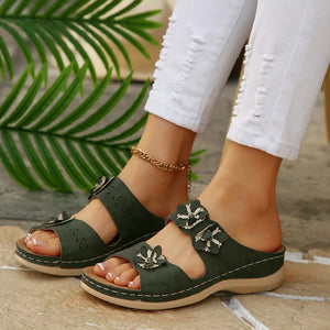 Army green slip-on sandals with floral appliqués and cutout details.