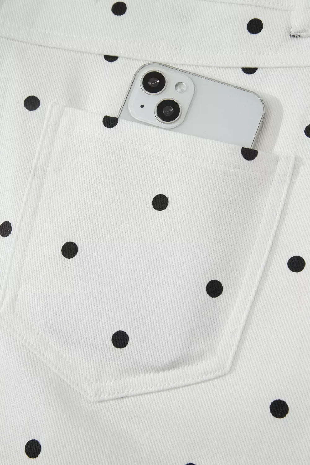 White chino shorts with black polka dots and a back pocket holding a smartphone.