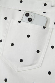 White chino shorts with black polka dots and a back pocket holding a smartphone.
