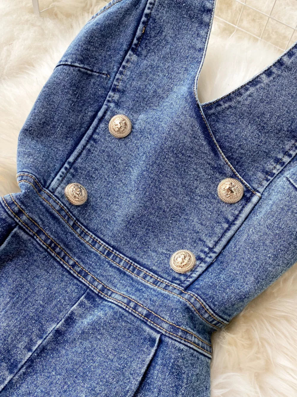 Blue denim halter jumpsuit with gold button detail and wide legs.