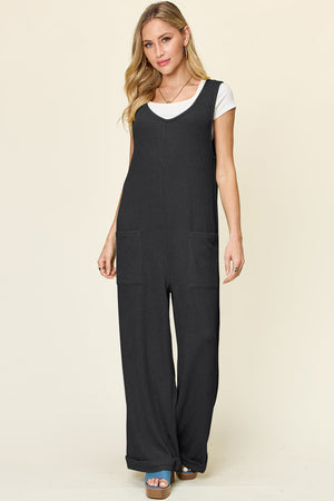 Black ribbed knit tie-strap jumpsuit with wide legs and patch pockets.