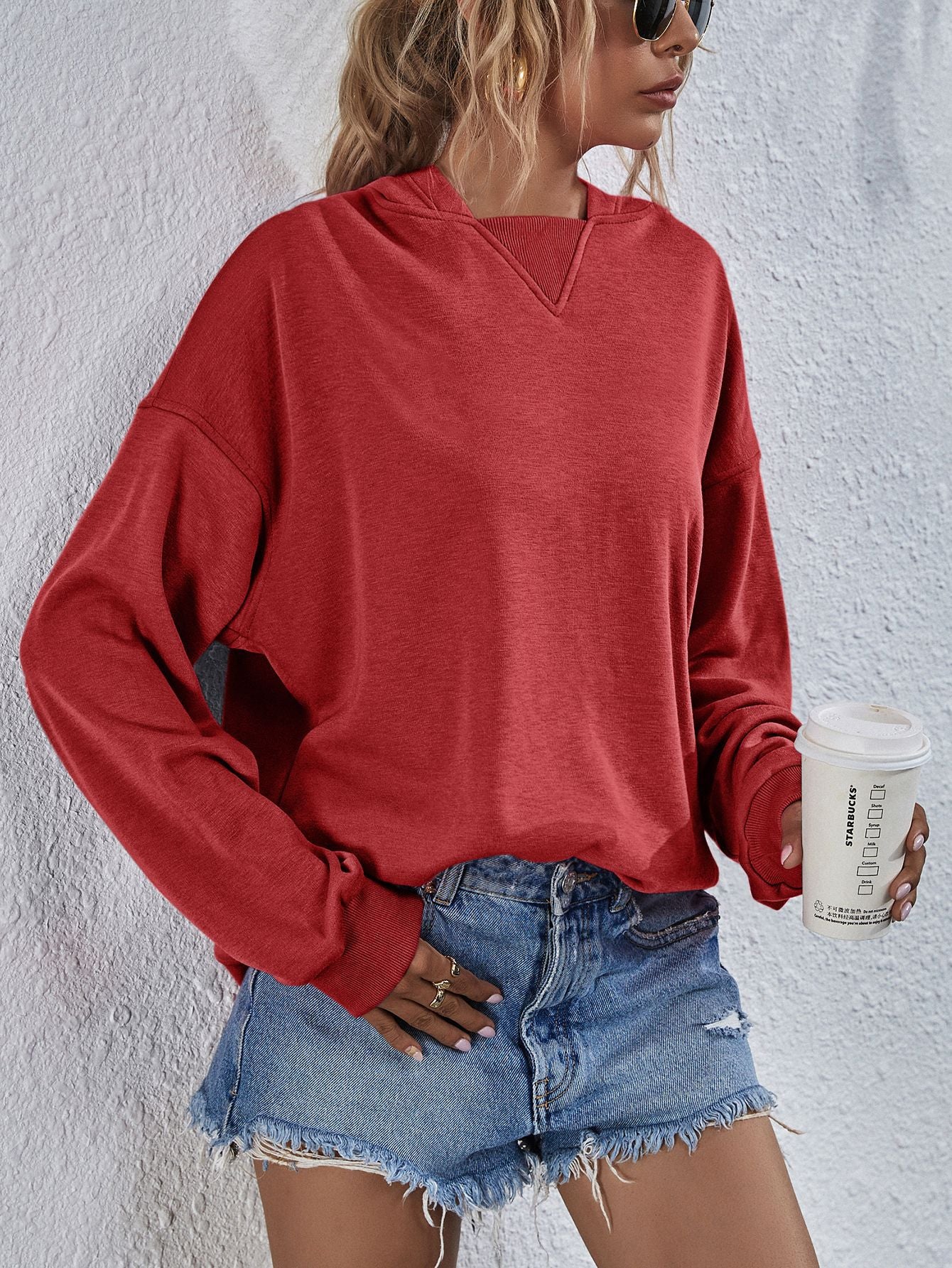 Boxy red sweatshirt with split hem neckline and ribbed cuffs, styled with denim shorts.