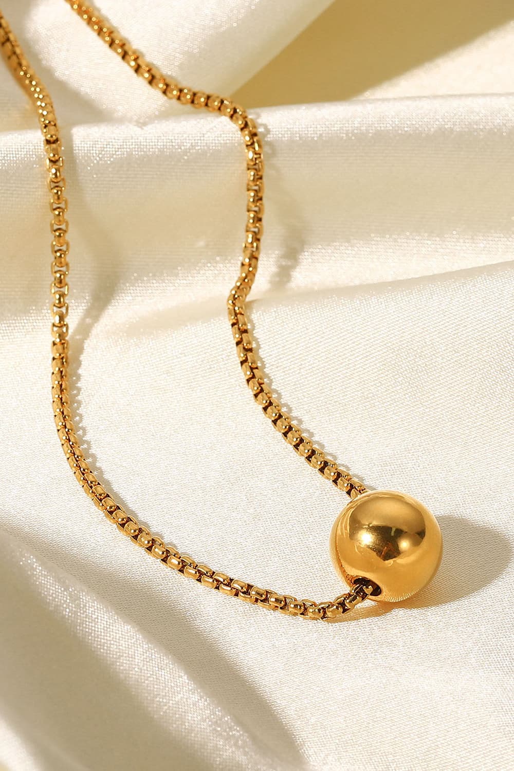 Gold orb pendant necklace with a box chain, on a satin background.