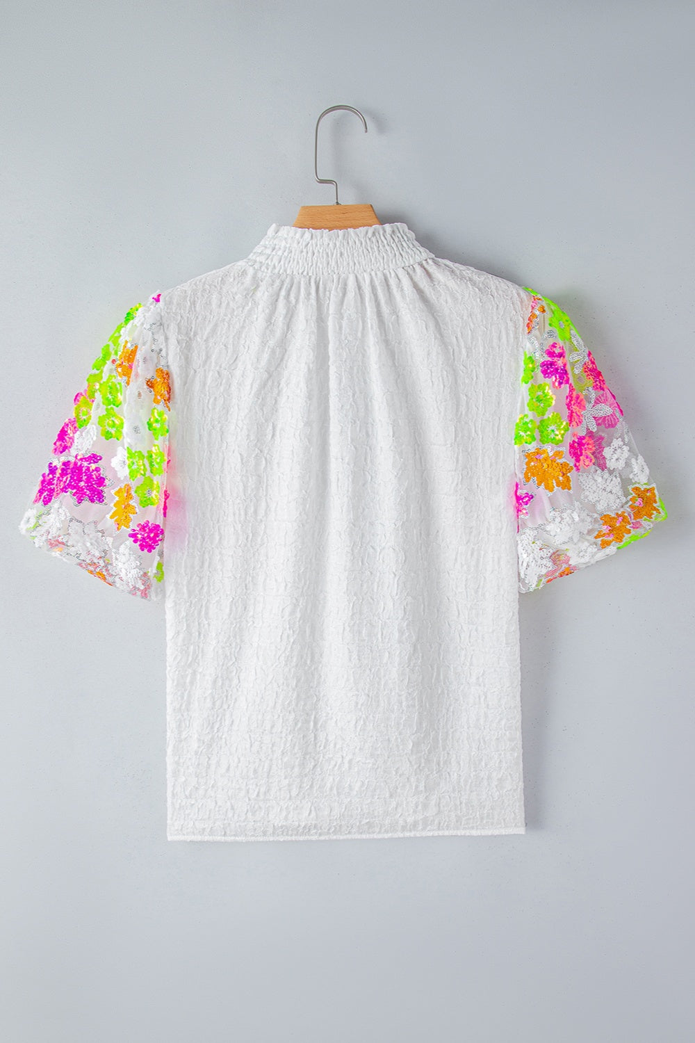 White textured blouse with colorful sequined floral puff sleeves and smocked neckline.