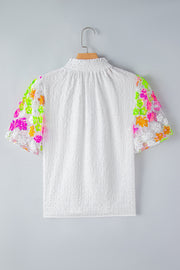 White textured blouse with colorful sequined floral puff sleeves and smocked neckline.