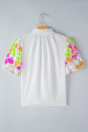 White textured blouse with colorful sequined floral puff sleeves and smocked neckline.
