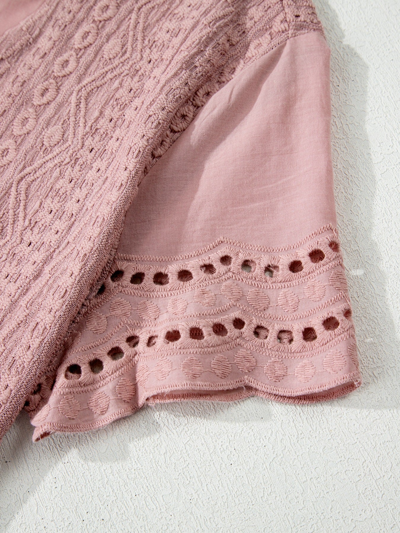 Pink eyelet embroidered short-sleeve blouse with intricate cutout details on the hem.