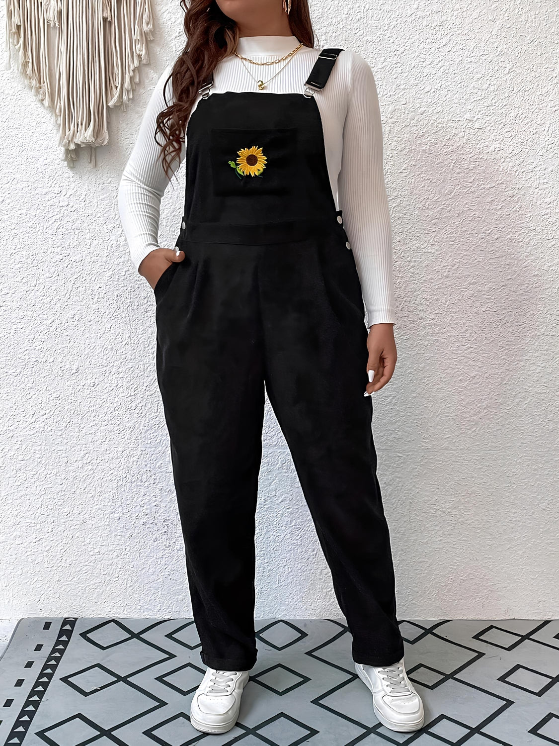 Black corduroy overalls with embroidered sunflower detail and relaxed fit.