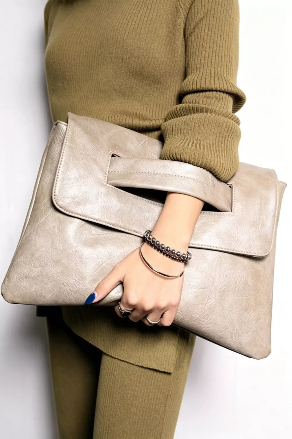 Light gray distressed leather envelope clutch with cut-out handle and silver bracelet.