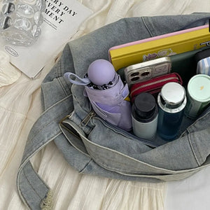 Washed denim hobo bag in medium blue, shown packed with essentials like a phone, wallet, and umbrella.