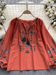 Orange red embroidered tie neck blouse with billowy sleeves and floral details.